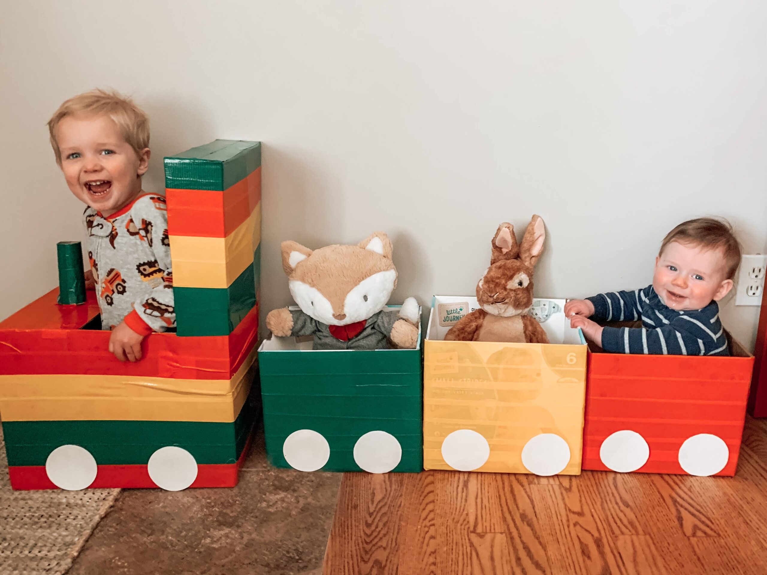 Kids playing with a repourposed cardboard train with stuffed animal and infant smiling enjoying the craft and activity